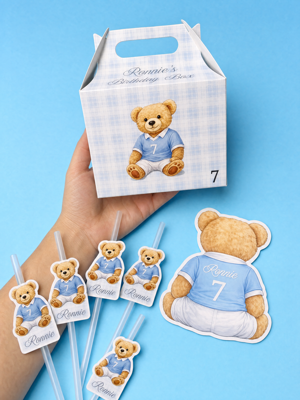 Hand holding a Ralph Lauren x Man City (designed by us) bear-themed birthday box with matching straw toppers and confetti on a blue background